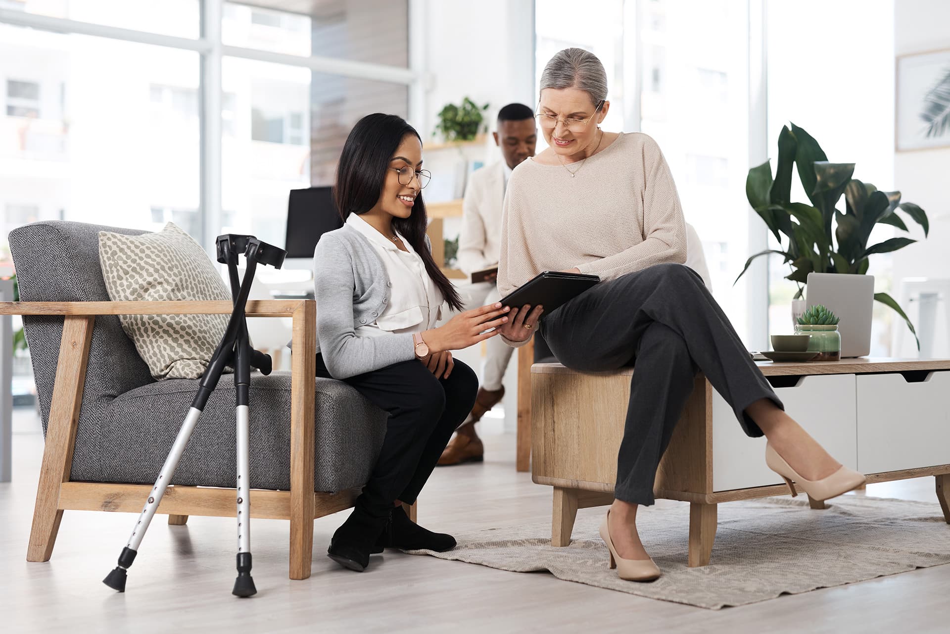 Office, team and happy women with tablet, crutches and article grammar check with glasses or editing. Creative, proofreading and person with disability, collaboration and review in publishing agency