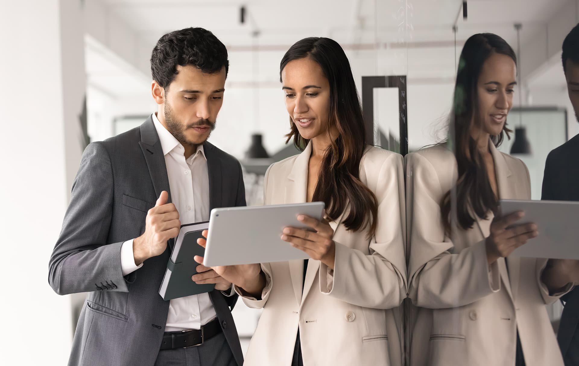 Two focused employees working on joint task or online presentation, exchanging ideas while using tablet device standing in corporate office. Modern technology, business digital tools usage, teamwork