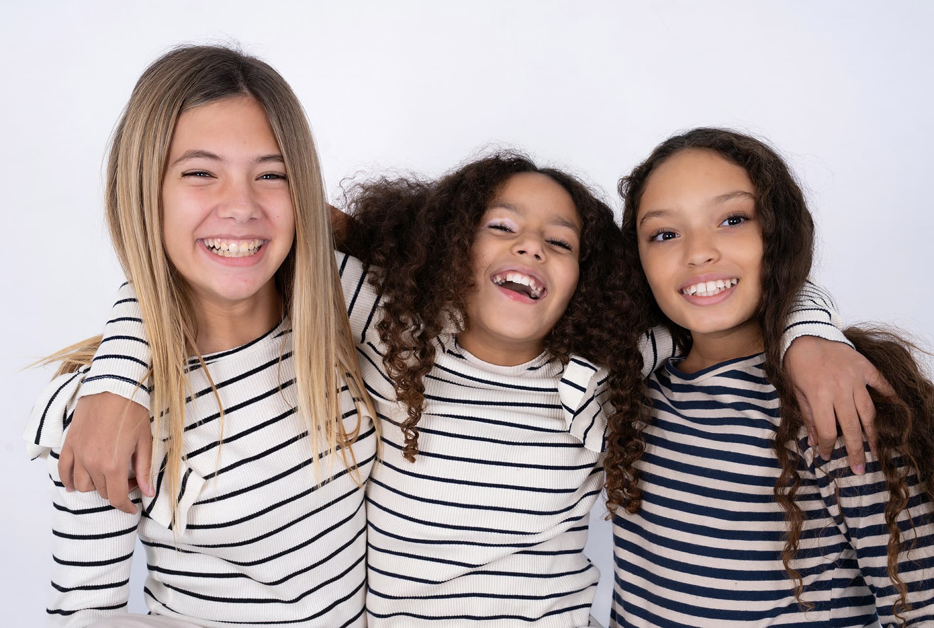 Three young multiracial kid girls hugging each other, having good time and playing.